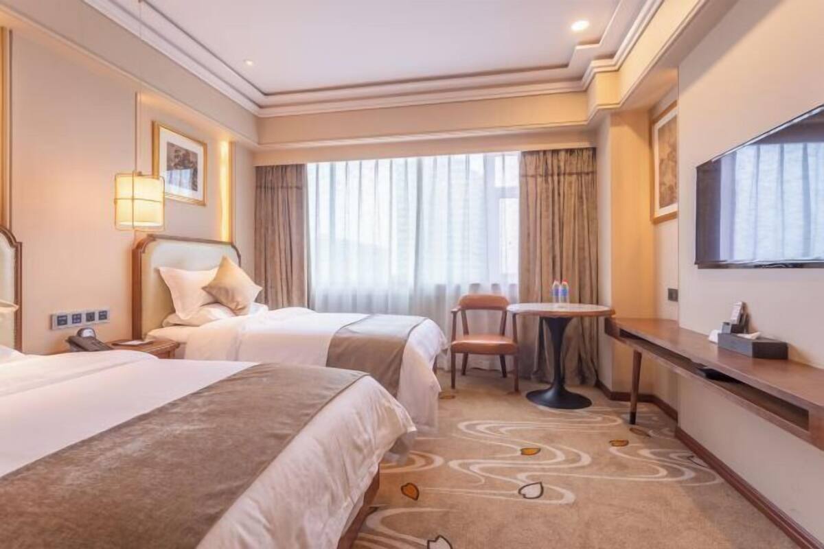 Een hotelkamer met twee bedden, een bureau, een stoel, een televisie en een raam met gordijnen.