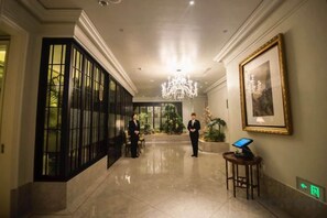 Vestíbulo de hotel con candelabro, una recepción y un amplio ventanal con vistas a zonas verdes.