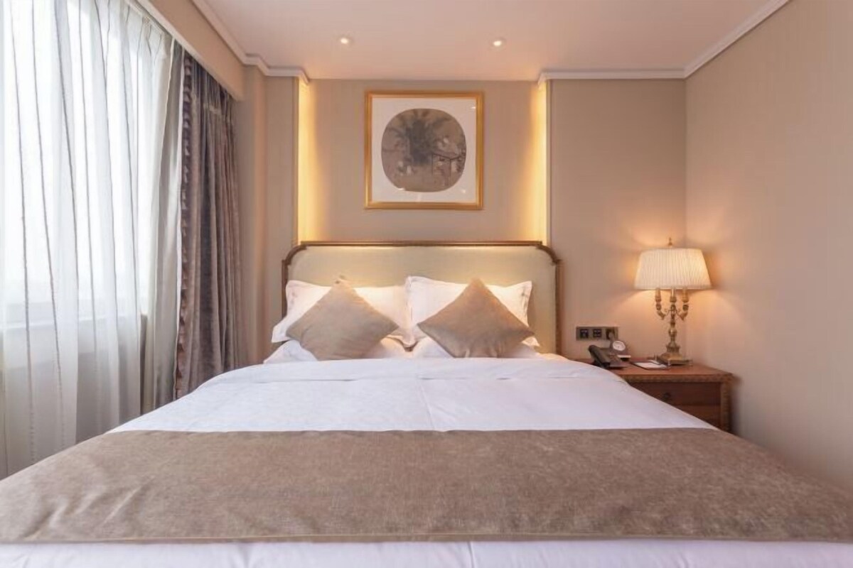 A hotel room with a bed, a bedside table with a lamp, and a framed picture on the wall.