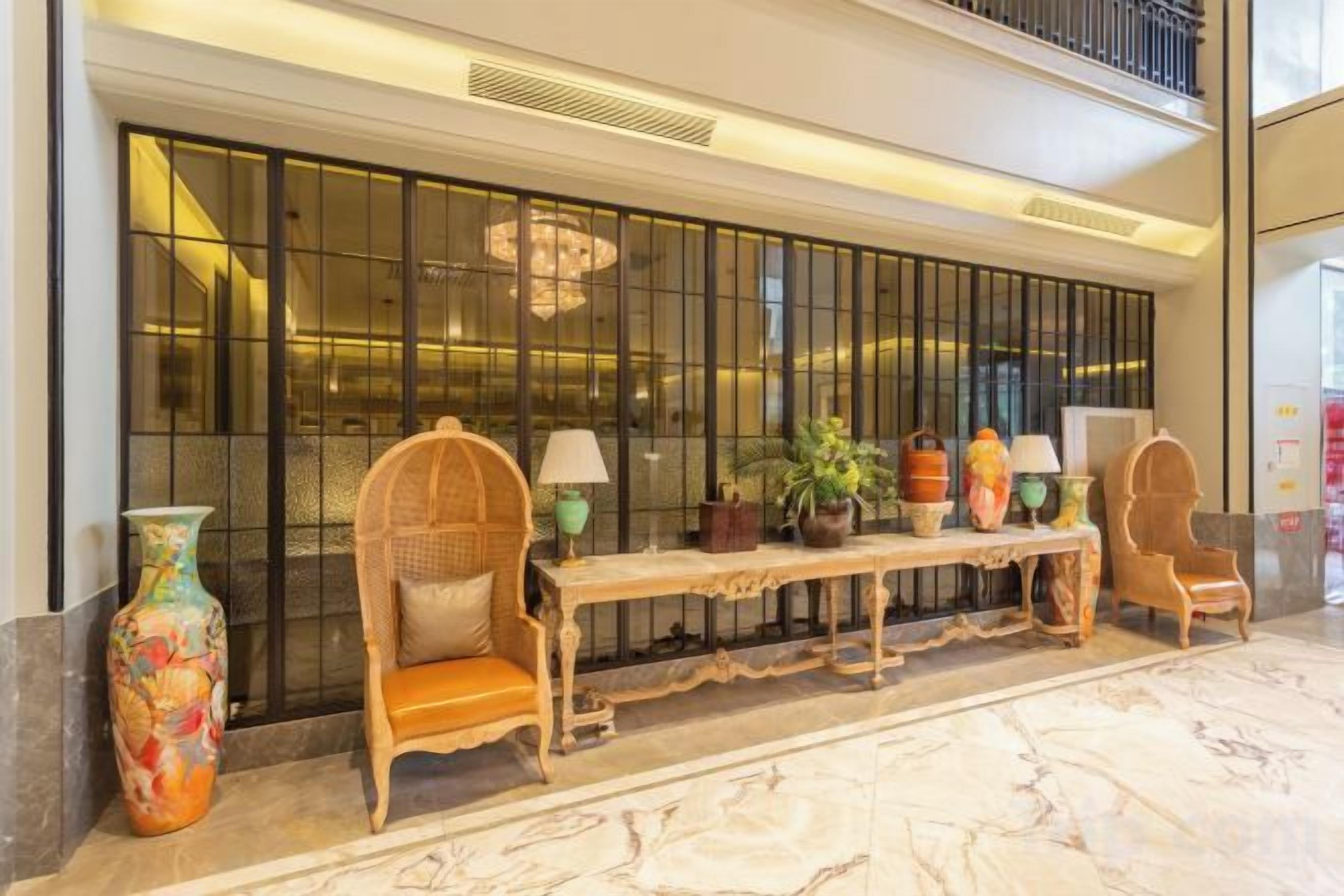 A lobby with a reception desk, two wicker chairs, a bench, and a large decorative vase.
