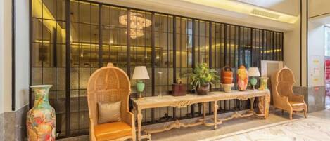 A lobby with a reception desk, two wicker chairs, a bench, and a large decorative vase.