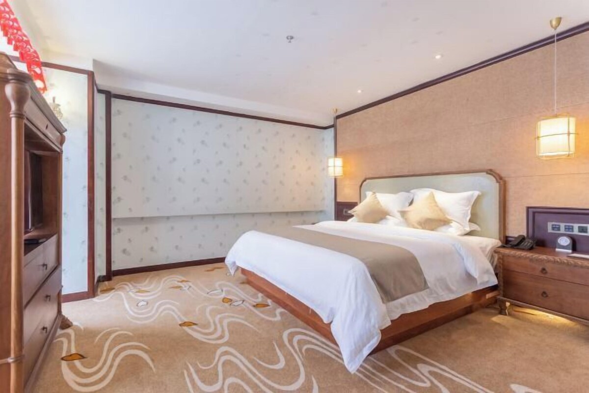 A hotel room with a bed, bedside table, lamp, and a patterned carpet.