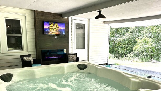 A hot tub with a television mounted on the wall, a door, and a view of trees outside.
