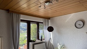 A room with a wooden ceiling, a large window with curtains, a standing floor lamp, a clock, and a radiator. - Vacation apartment "Pingo" Address: Bundesstraße 1, 53506 Ahrbrück!  (Ahrbrück)
