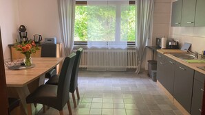 A modern kitchen with a dining area, featuring a window with curtains, a radiator, and various kitchen appliances. - Vacation apartment "Pingo" Address: Bundesstraße 1, 53506 Ahrbrück!  (Ahrbrück)