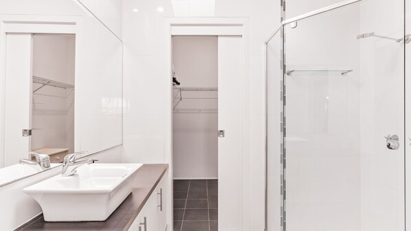 Une salle de bain moderne avec un grand miroir, un lavabo blanc et une douche à parois de verre.