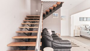 Un interno moderno con una scala in legno, un divano in pelle e un letto con copriletto fantasia.