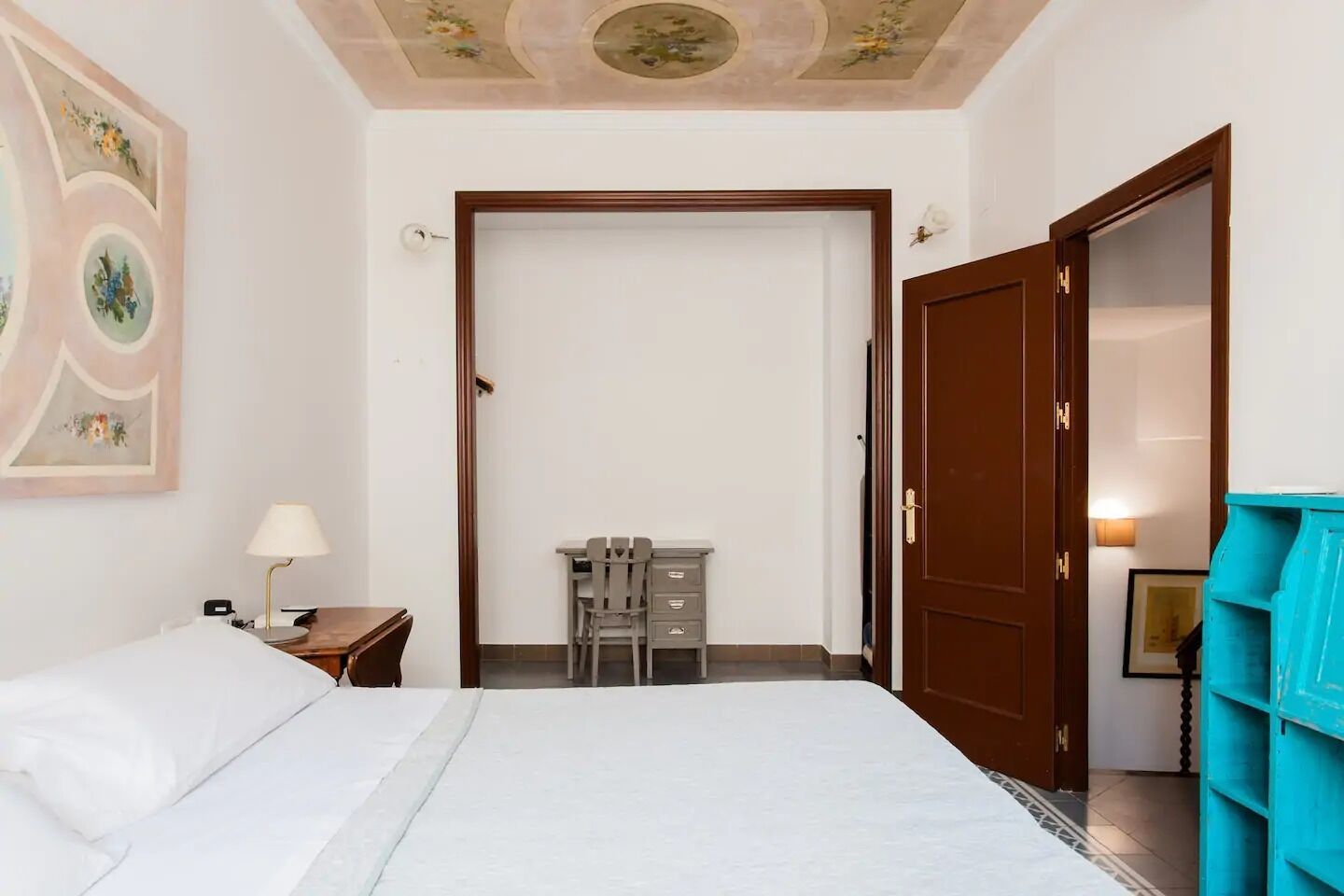 Habitación de hotel con cama, escritorio con silla, armario y puerta que da a otra habitación.