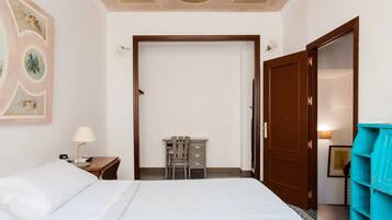Habitación de hotel con cama, escritorio con silla, armario y puerta que da a otra habitación.