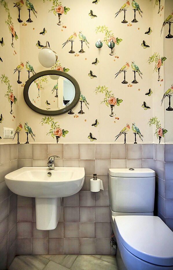 A bathroom with a sink, toilet, and mirror. The walls are decorated with bird and flower patterns.