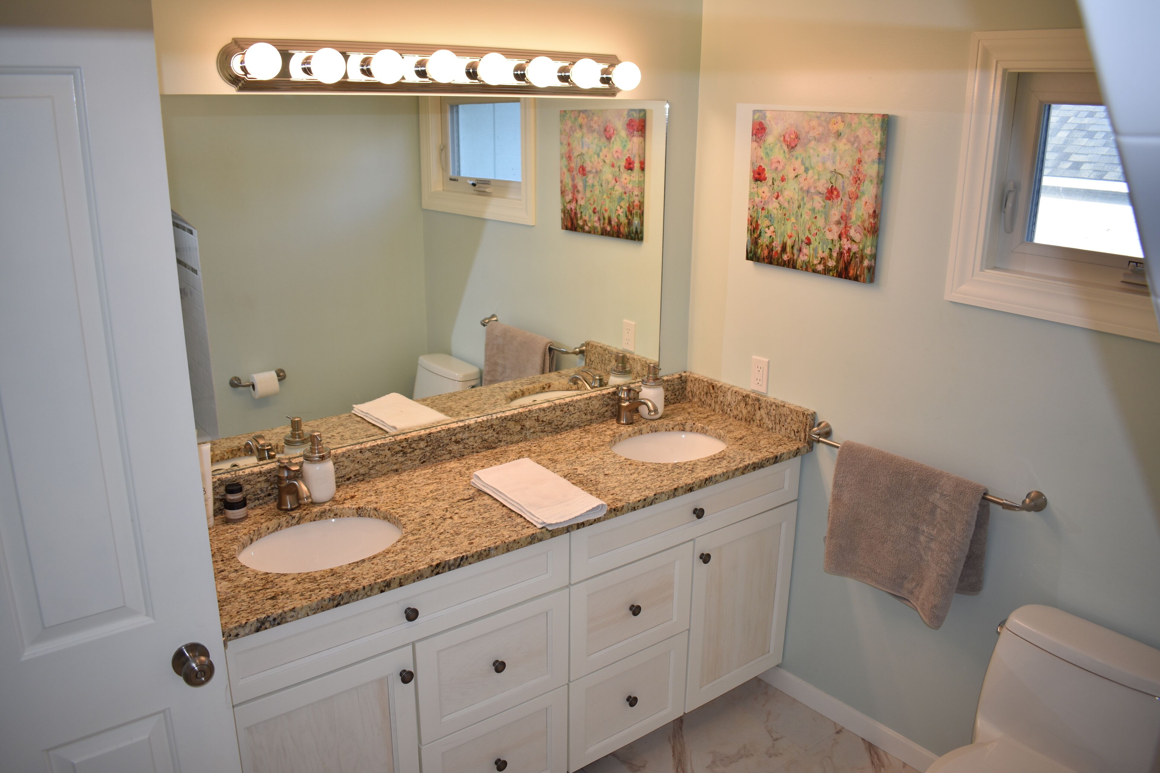 A bathroom with two sinks, a vanity with drawers, a towel rack, and a toilet.