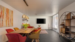 A modern dining area with a wooden table, red and yellow chairs, a vase of tulips, and a large abstract painting on the wall.