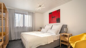 A modern bedroom with a bed, a bedside table with a lamp, a yellow chair, and a red abstract painting on the wall.
