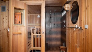 A wooden sauna with a control panel, a shower area with a tiled wall, and a wooden bench.