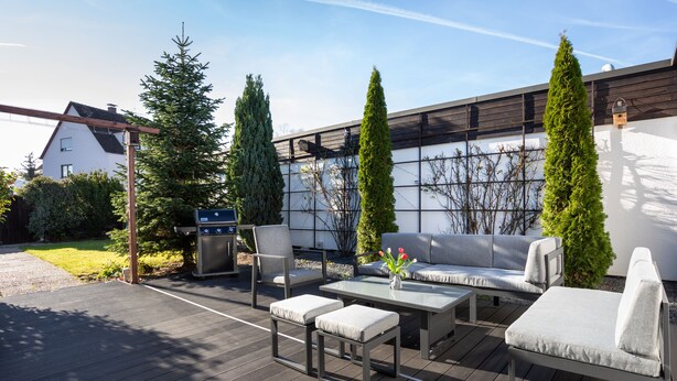 An outdoor patio with a grill, seating area, and tall trees.