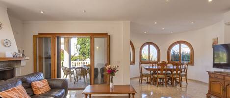 A spacious living room with a leather sofa, a wooden dining table, and a TV.