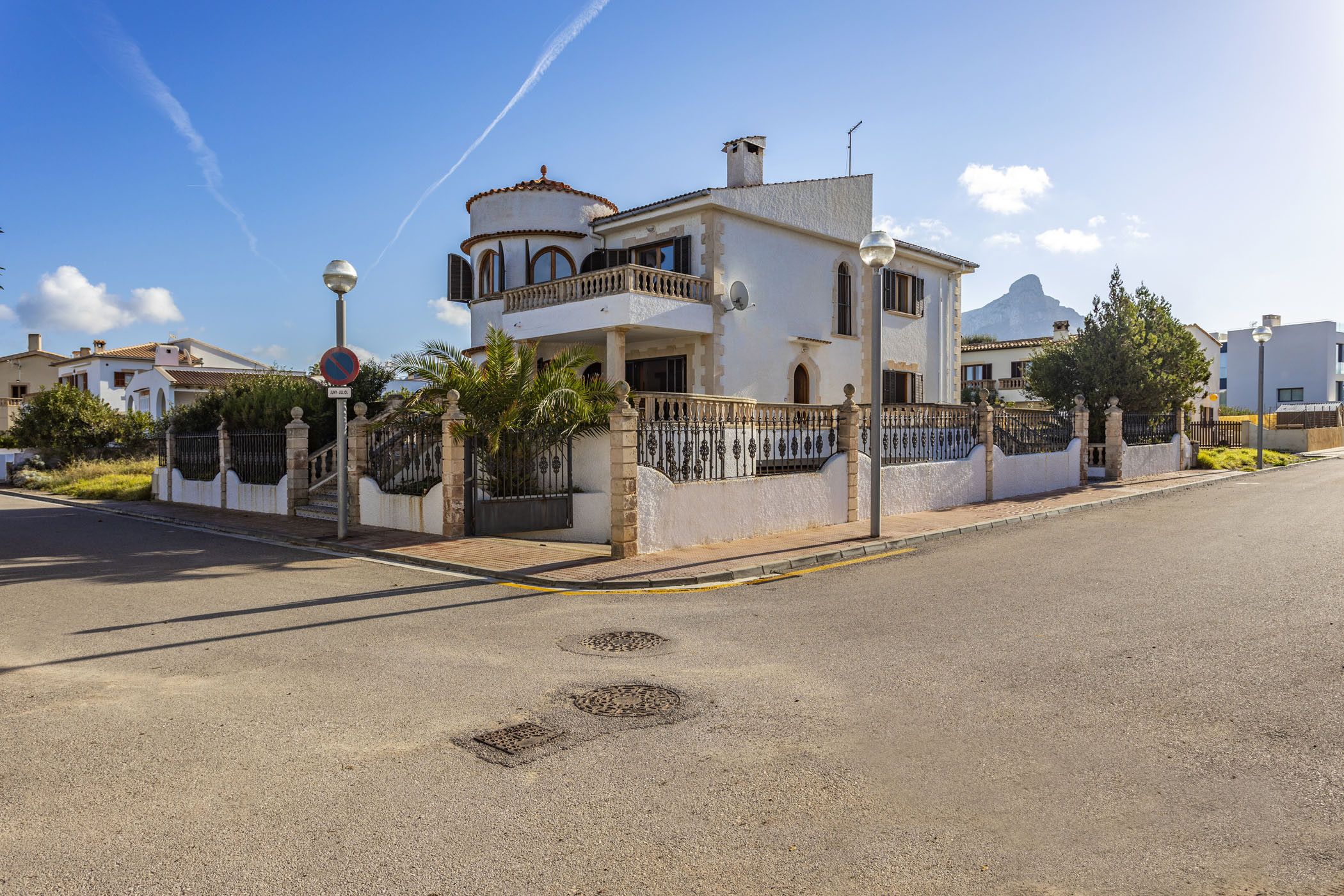A two-story house with a balcony, a gated entrance, and a mountain in the background.