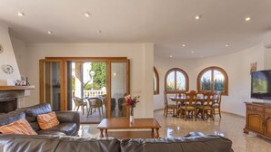A spacious living room with a leather sofa, a wooden dining table, and a TV. - Villa by the sea with 4 bedrooms, 2 bathrooms, barbecue and terraces (Colonia de Sant Pere)