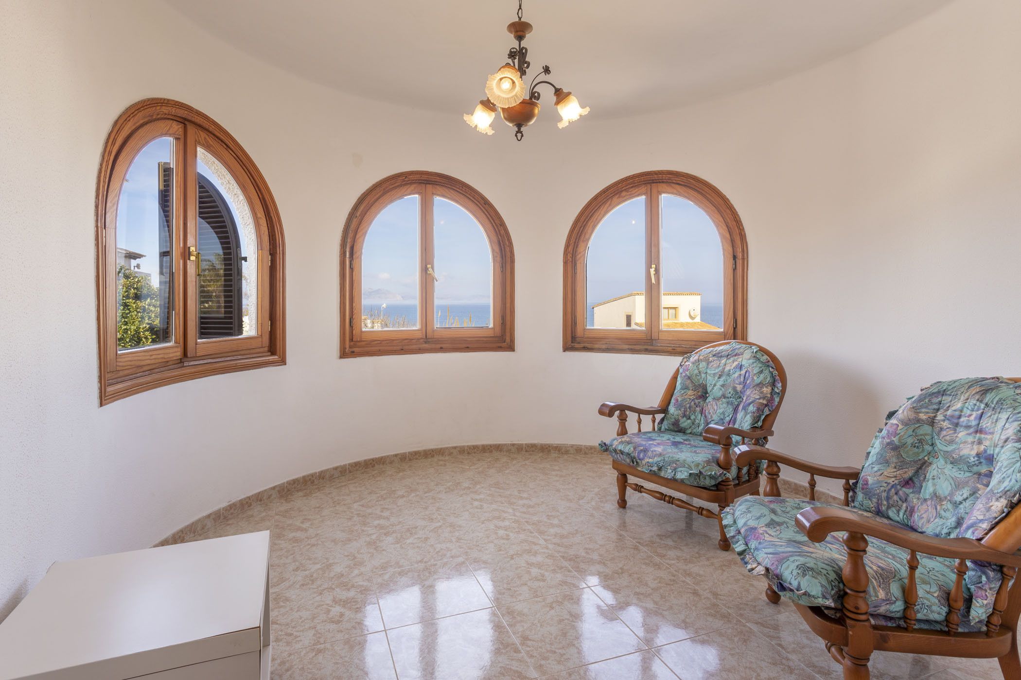 A spacious room with three arched windows, a chandelier, and two upholstered chairs.
