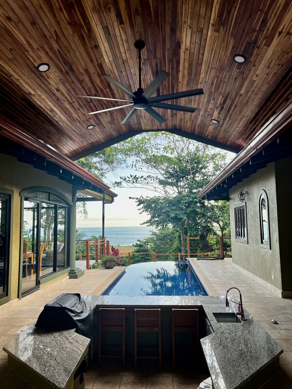A pool area with a ceiling fan, a view of the ocean, and a seating area with a table and chairs. - ★Sophisticated Costa Rica Getaway: Spacious, Exclusive, and Luxurious★ (Jaco)