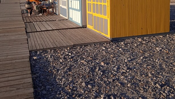 Une rangée de cabanes de plage, reliées par une passerelle en bois.
