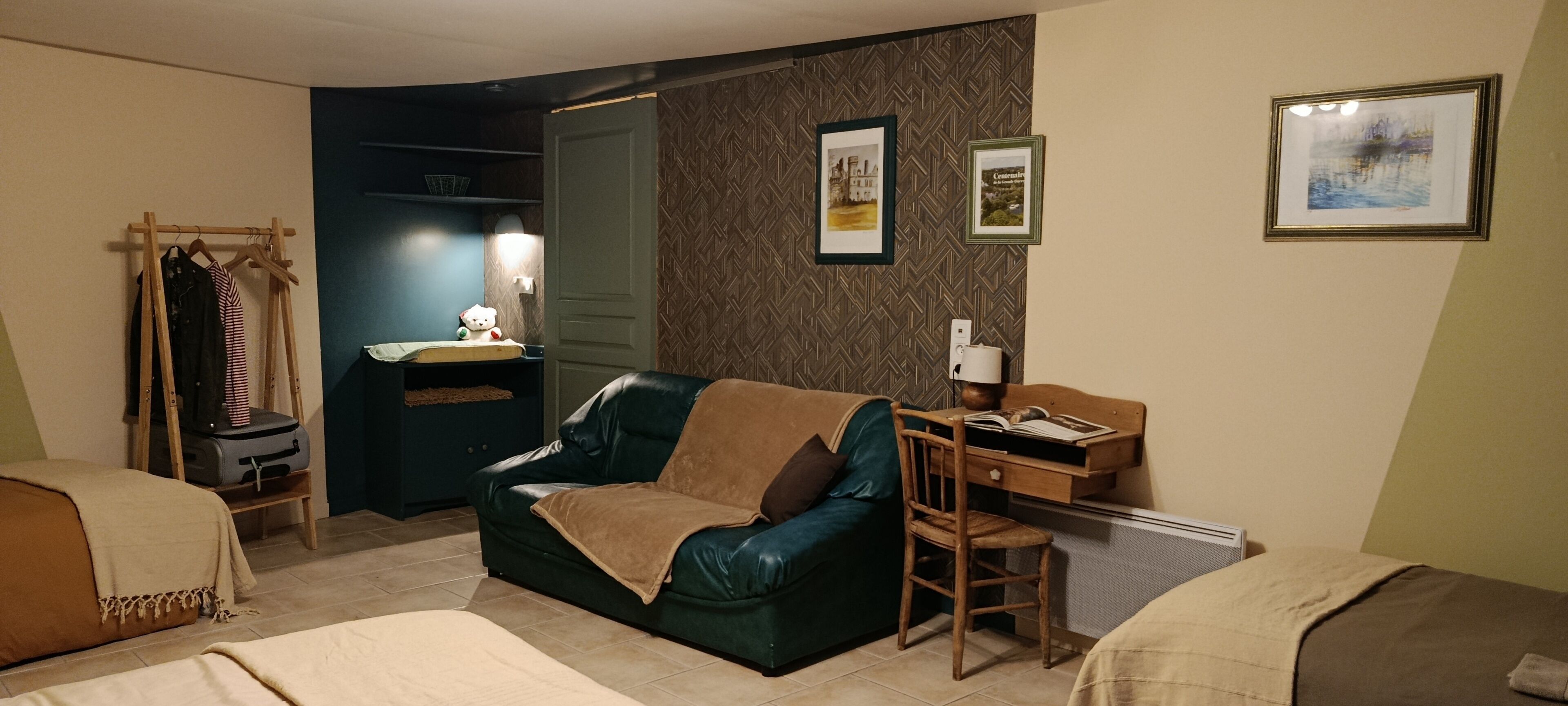 A hotel room with a leather sofa, a desk with a chair, a wardrobe, and two beds.