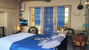 Une chambre à coucher avec un lit, une télévision, une cheminée et une vue sur l’extérieur à travers des rideaux bleus.