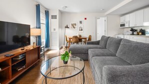Ein modernes Wohnzimmer mit einem Flachbildfernseher, einem Glastisch und einem grauen Ecksofa.