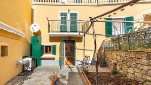 A courtyard with a stone wall, a wooden bench, and a door leading to a balcony. - Bright Finalborgo Apartment - BBQ, Bike Storage, Garden (Finale Ligure)