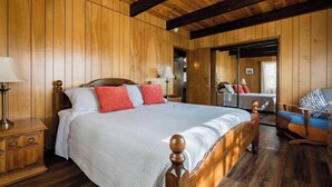 A wooden-paneled bedroom with a large bed, a nightstand, a chair, and a mirror. - Cabin that features modern upgrades near Snow & Play (Big Bear)