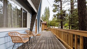 A wooden deck with two wicker chairs, a wooden railing, and a view of a forested area. - Cabin that features modern upgrades near Snow & Play (Big Bear)
