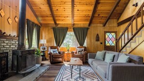 A cozy cabin interior with a fireplace, wooden walls, a sofa, and a dining table. - Cabin that features modern upgrades near Snow & Play (Big Bear)
