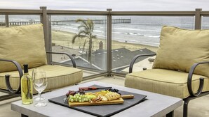 Een balkon met een tafel gedekt voor een maaltijd, met uitzicht op een strand en een pier.