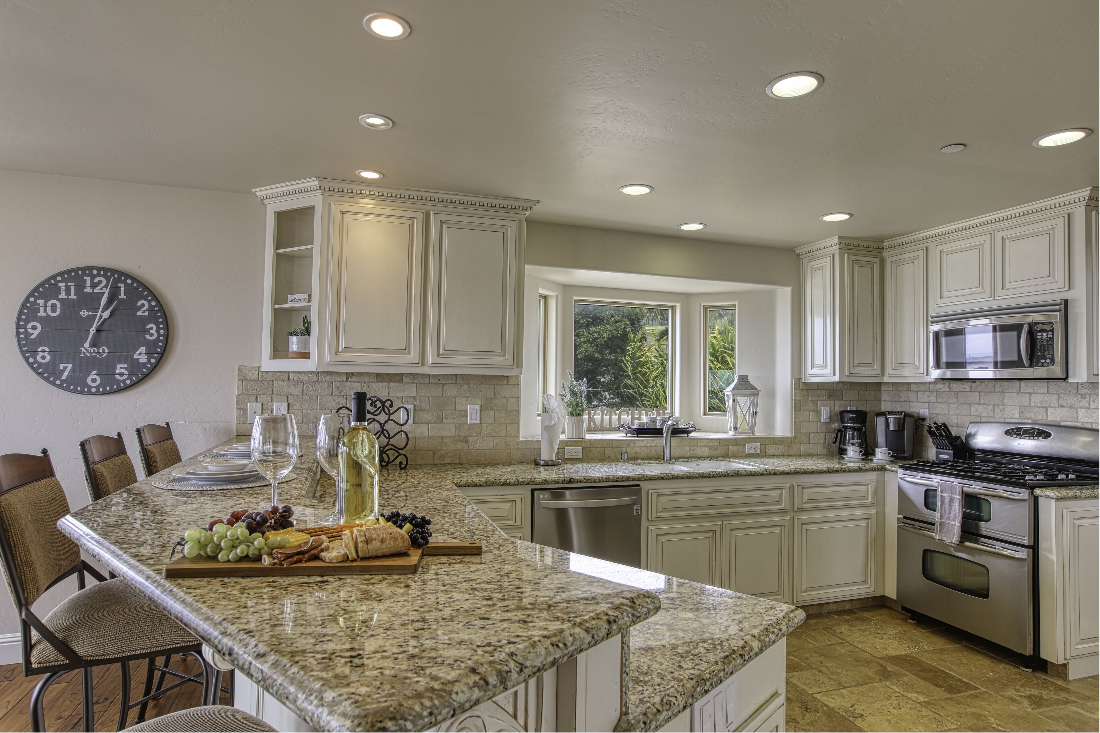 A kitchen with white cabinets, a granite countertop, a stainless steel oven, and a clock on the wall.