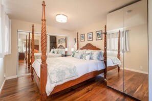 A spacious bedroom with a four-poster bed, a large mirror, and a wooden floor.