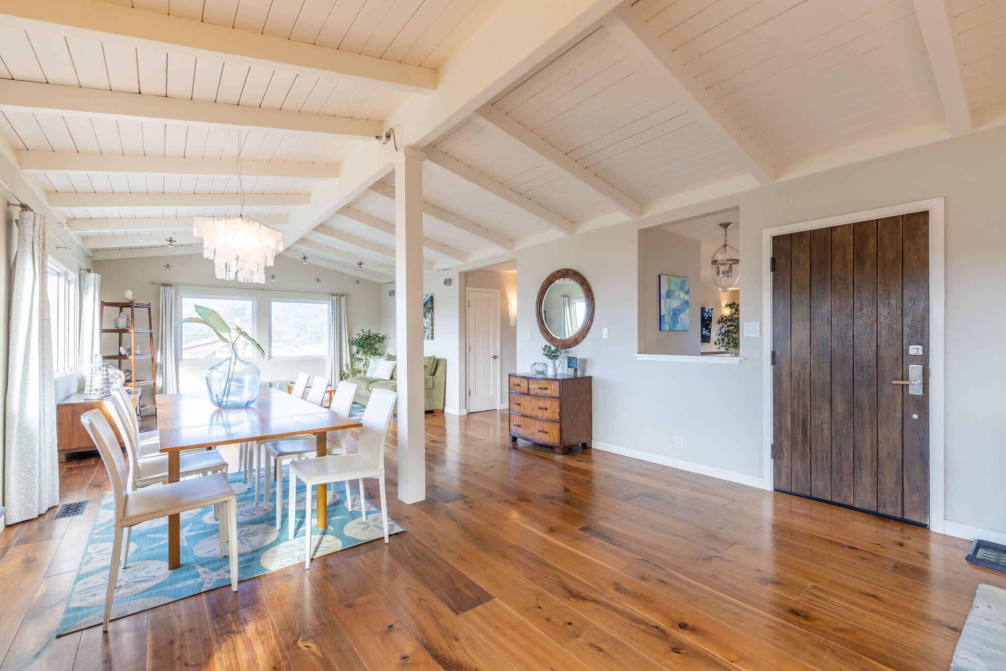 A spacious room with wooden flooring, a dining area with a table and chairs, a large mirror, and a wooden door.