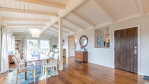 A spacious room with wooden flooring, a dining area with a table and chairs, a large mirror, and a wooden door. - Ocean & Mountain View Home - Walk to Trails, Beach, Family Activities (Montara)