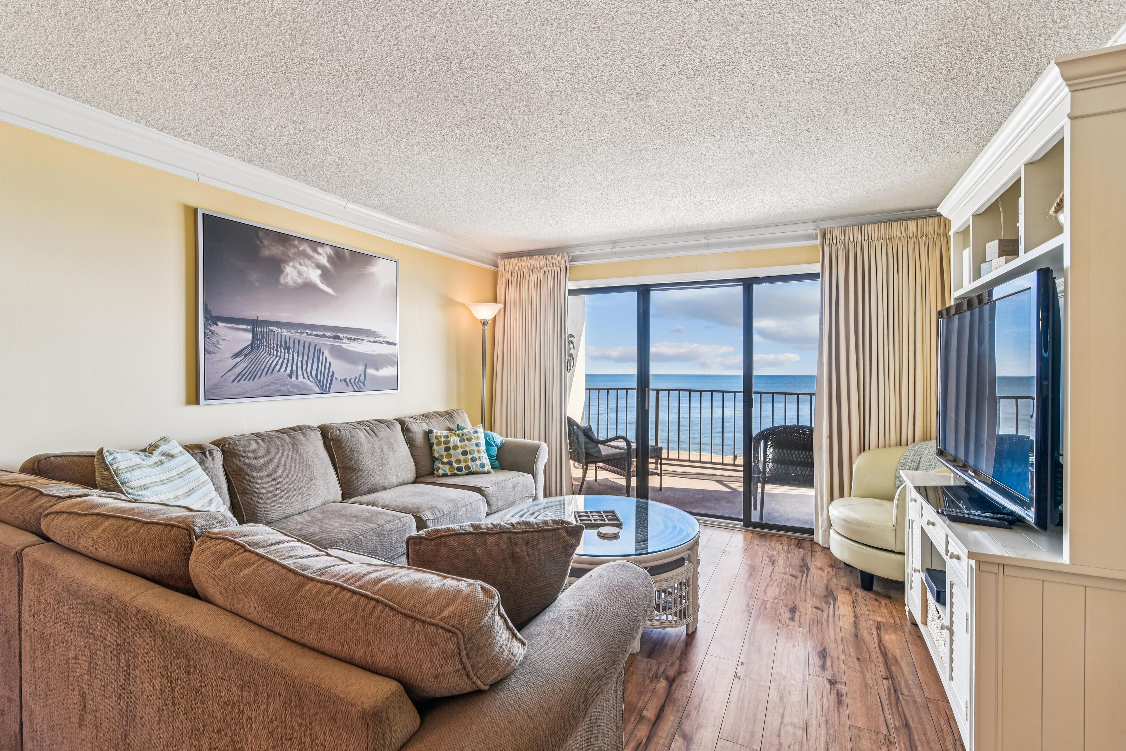 Un salon avec un canapé, une table basse et un téléviseur. Il y a un balcon avec vue sur l’océan.