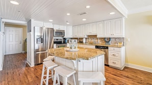 A kitchen with white cabinetry, a granite countertop island, and wooden flooring. - DAILY ACTIVITIES & LINENS INCLUDED*! Lovely direct Oceanfront, 2 bedroom (Den converted to a third bedroom, there is a pocket door for privacy with a queen bed, closed from kitchen but open to entry) 2 bath condo. (Ocean City)
