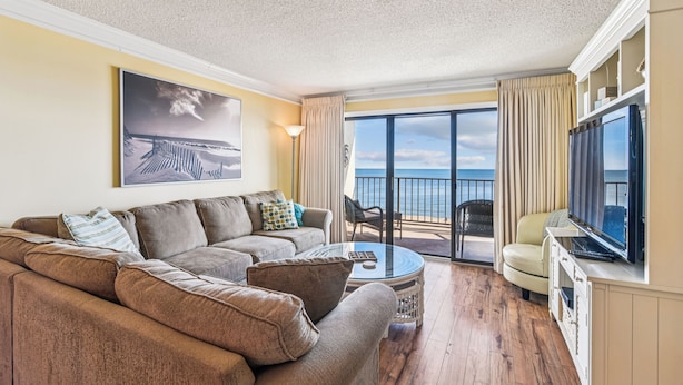 A living room with a sofa, a coffee table, a TV, and a balcony with a view of the sea. - DAILY ACTIVITIES & LINENS INCLUDED*! Lovely direct Oceanfront, 2 bedroom (Den converted to a third bedroom, there is a pocket door for privacy with a queen bed, closed from kitchen but open to entry) 2 bath condo. (Ocean City)