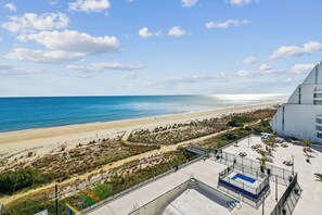 A beach view with a pool, a fenced area with plants, and a building with a sloped roof.