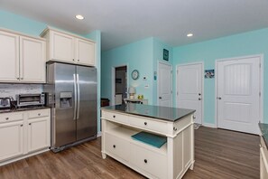 A kitchen with white cabinetry, a stainless steel refrigerator, a built-in oven, and a small island with a sink. - Dawn By The Bay-Designer Decor with Great Ocean Views, Sleeps 12 (Surf City)