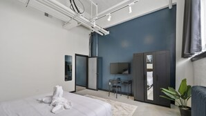 A modern hotel room with a bed, a desk, a TV, and a wardrobe. - Industrial Loft 5 min to Children’s Hospital, slps 4 (Pittsburgh)