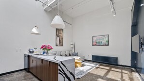 A modern kitchen with a marble island, pendant lighting, and a living area with a sofa and a coffee table. - Industrial Loft 5 min to Children’s Hospital, slps 4 (Pittsburgh)
