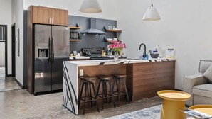 A modern kitchen with a stainless steel refrigerator, wooden cabinets, a built-in oven, and a bar area with stools. - Industrial Loft 5 min to Children’s Hospital, slps 4 (Pittsburgh)