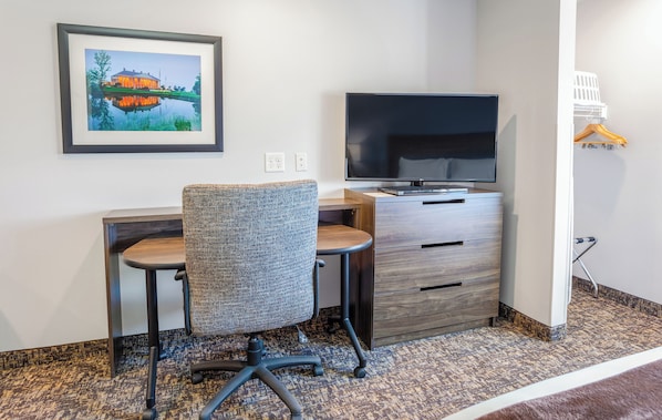 A hotel room with a desk, chair, TV, and a framed picture on the wall.