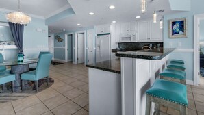 A modern kitchen with white cabinets, a granite countertop, and teal bar stools.