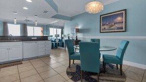 A modern kitchen with white cabinets, a granite countertop, and a dining area with teal chairs and a round table.
