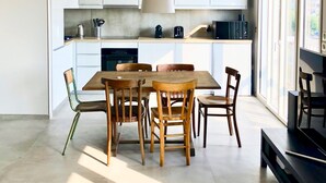A modern kitchen with white cabinets, a wooden dining table, and a pendant light. - TROUVILLE 3 Bdrms 65m2 SPLENDID AND CLEAR VIEW, BATHED IN LIGHT (Trouville-sur-Mer)