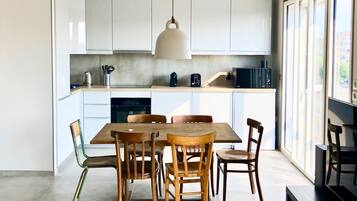 Une cuisine moderne avec des meubles blancs, une table à manger en bois et un luminaire suspendu.